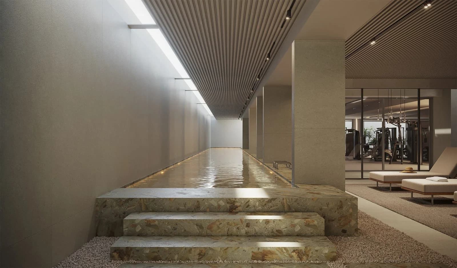 Imagem de piscina com raia em ambiente interno, revestimento em mármore terrazzo, teto com iluminação zenital e academia envidraçada ao fundo, com espreguiçadeiras.
